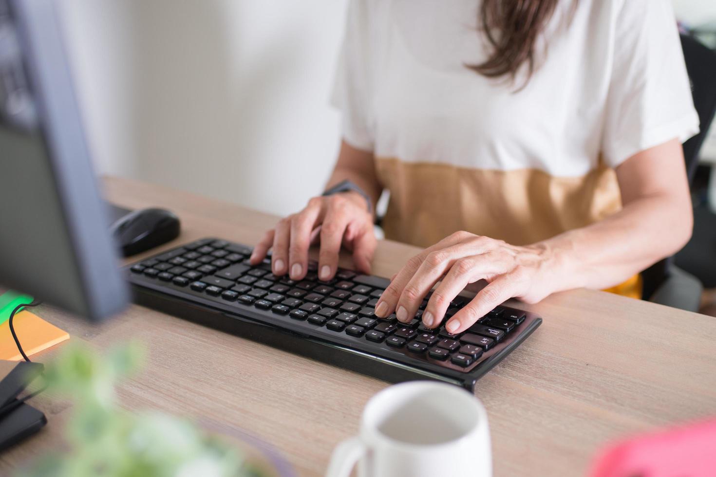 gros plan d'une femme travaillant à la maison. mains sur le clavier. tasse blanche et une plante sur le bureau photo