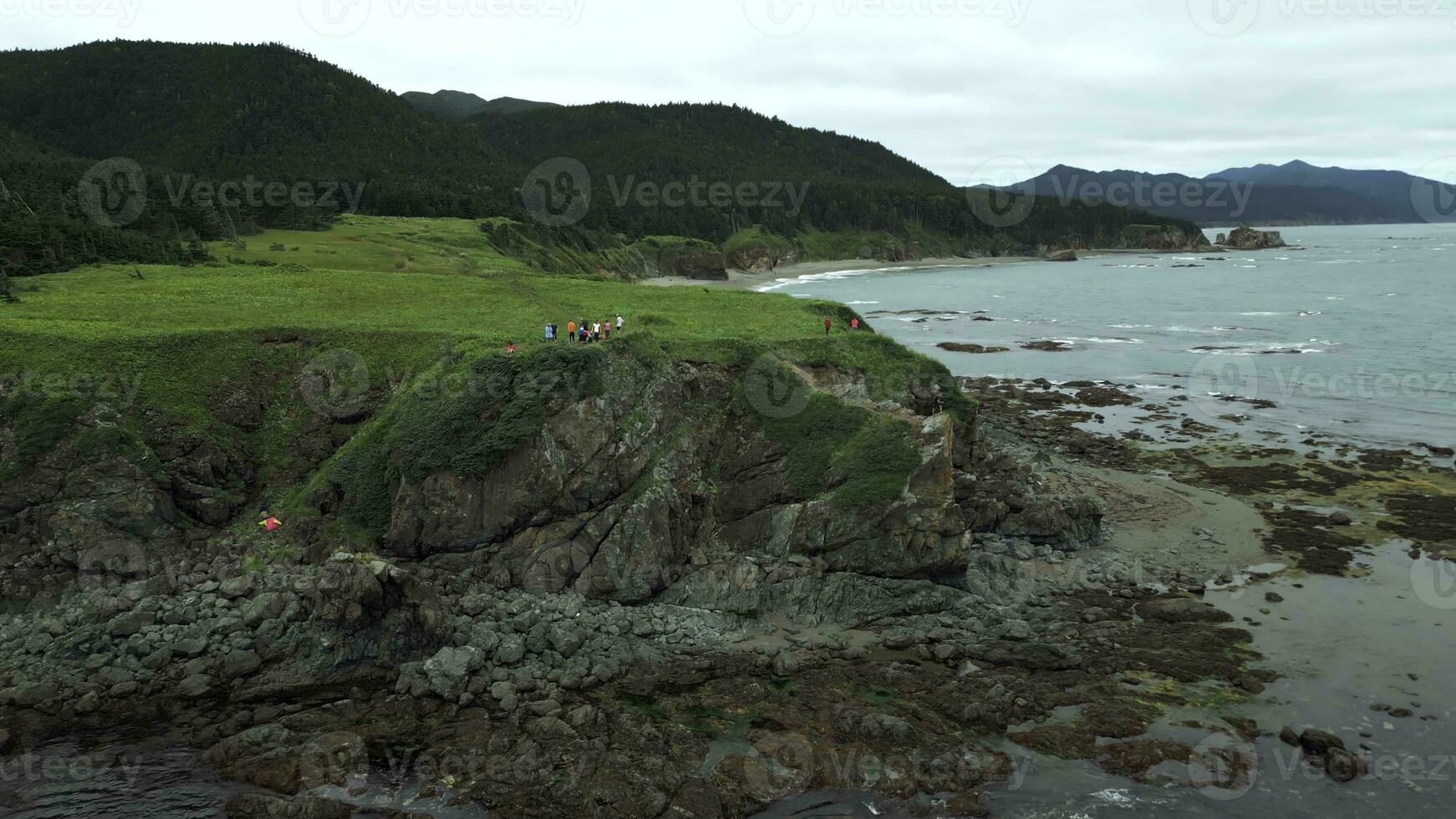 Haut vue de groupe de touristes sur bord de mer falaise. agrafe. randonneurs sur bord de rocheux littoral. touristes sur bord de falaise de rivage sur nuageux journée photo