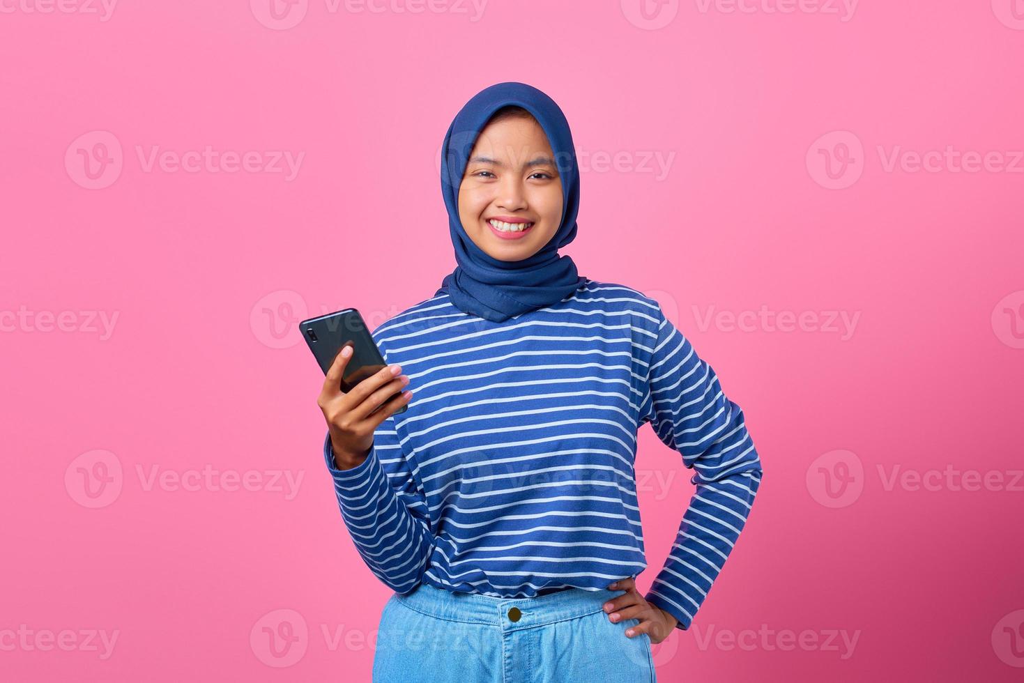 Portrait d'une jeune femme asiatique heureuse tenant un smartphone sur fond rose photo