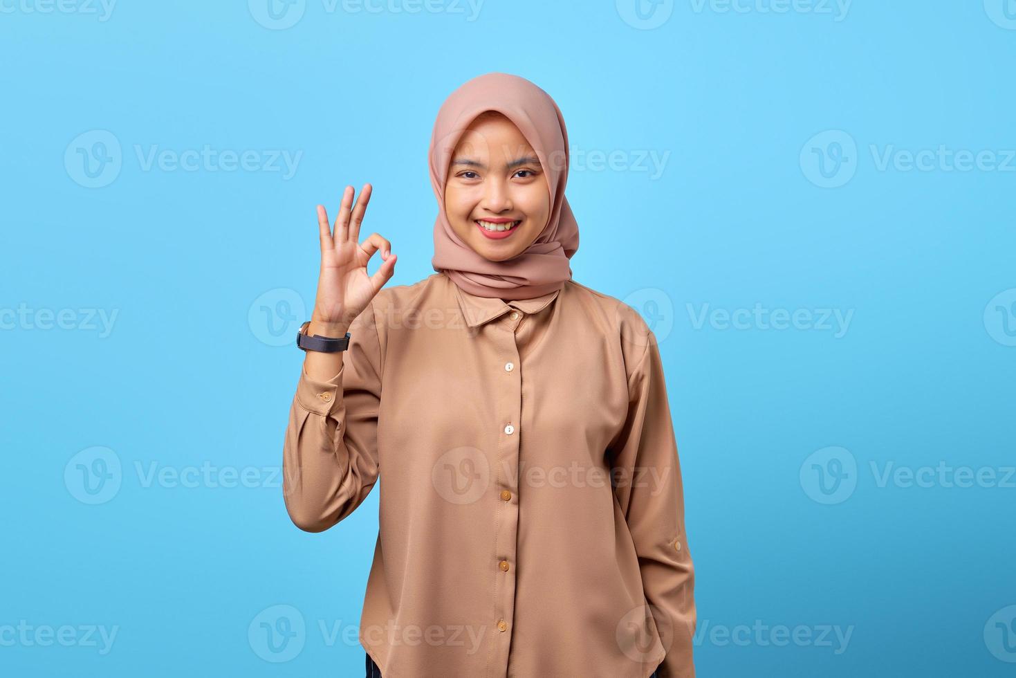 Portrait de jeune femme asiatique souriante faisant signe d'accord avec les mains du doigt sur fond bleu photo