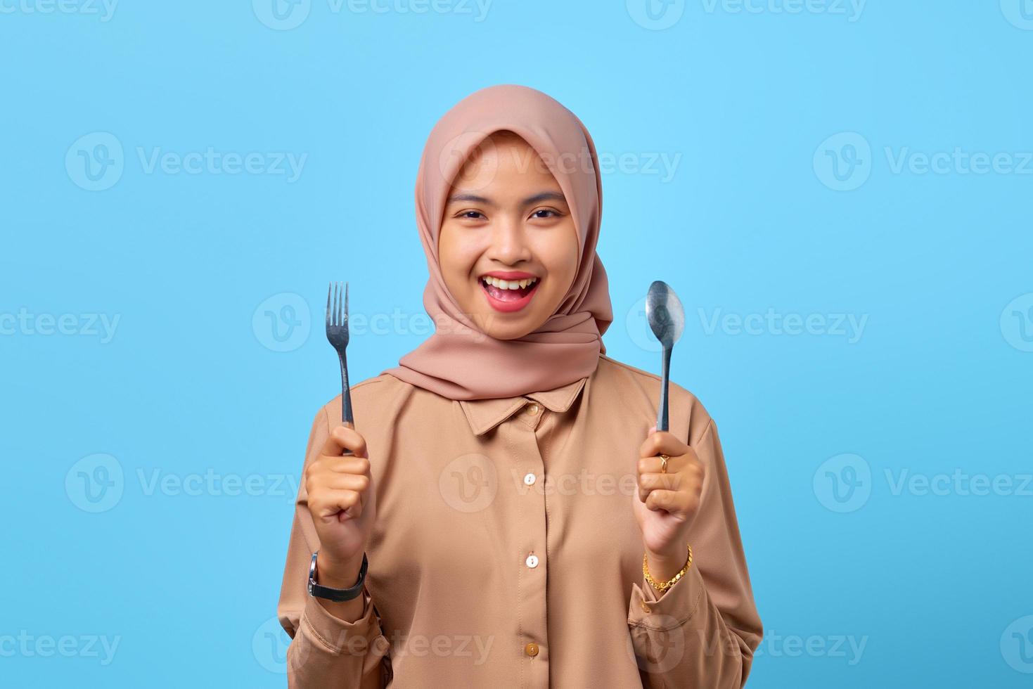 Portrait de jeune femme asiatique souriante tenir une fourchette et une cuillère sur fond bleu photo