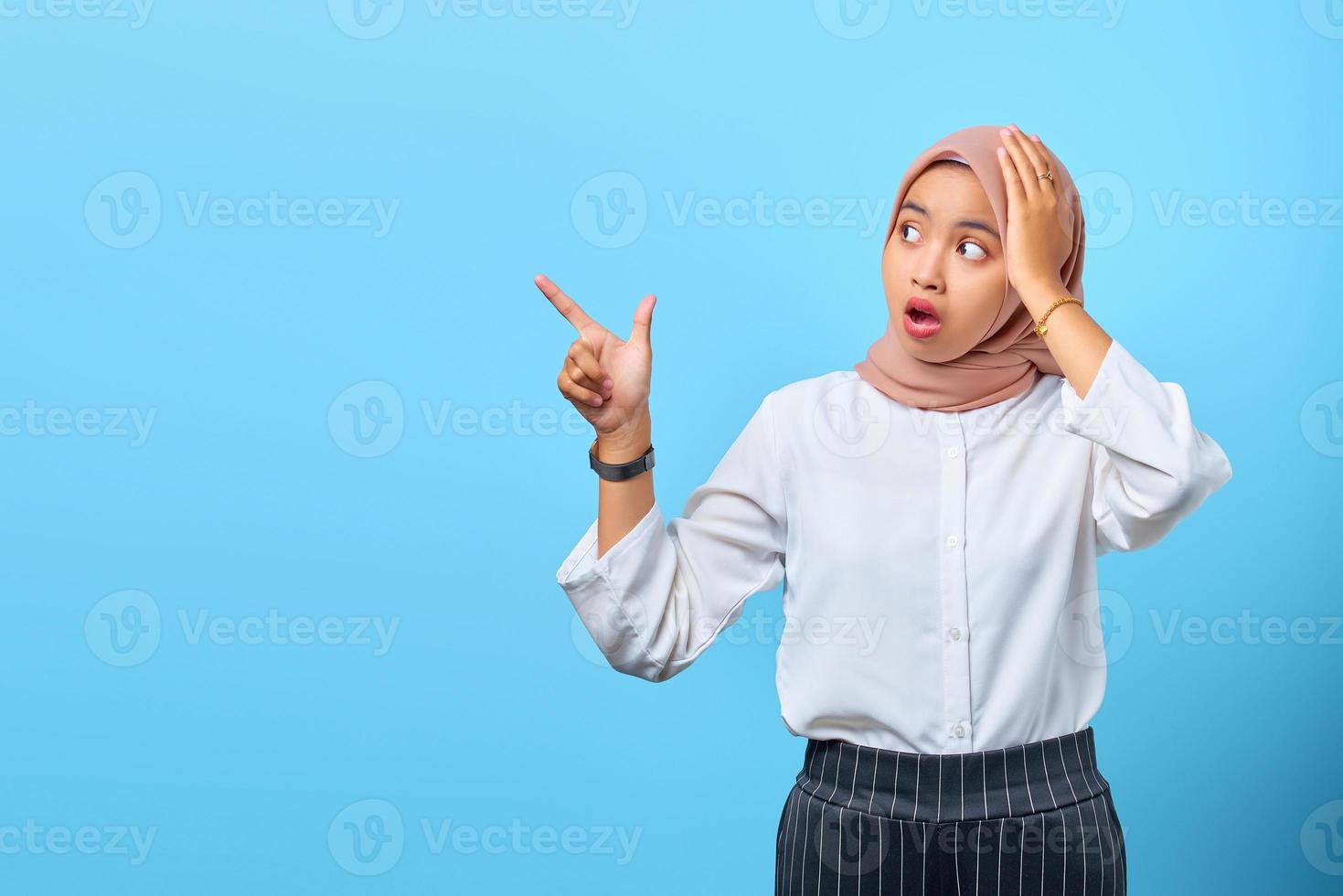 portrait d'une jeune femme asiatique surprise pointant vers un espace vide avec la bouche ouverte photo