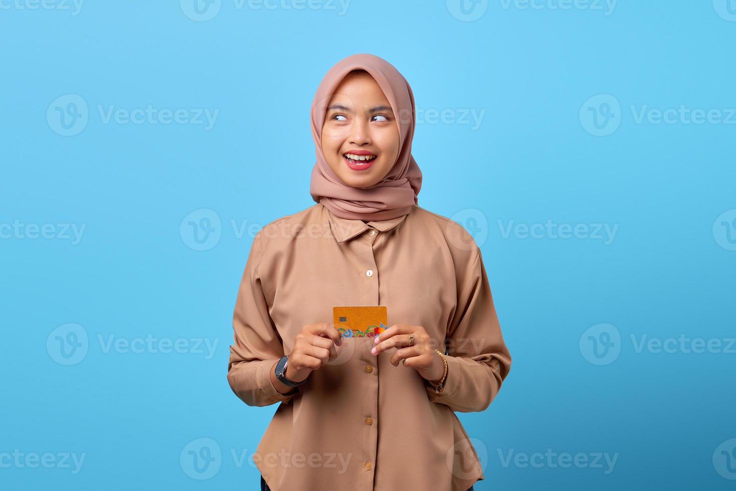 Portrait d'une jeune femme asiatique souriante tenant une carte de crédit tout en regardant de côté photo