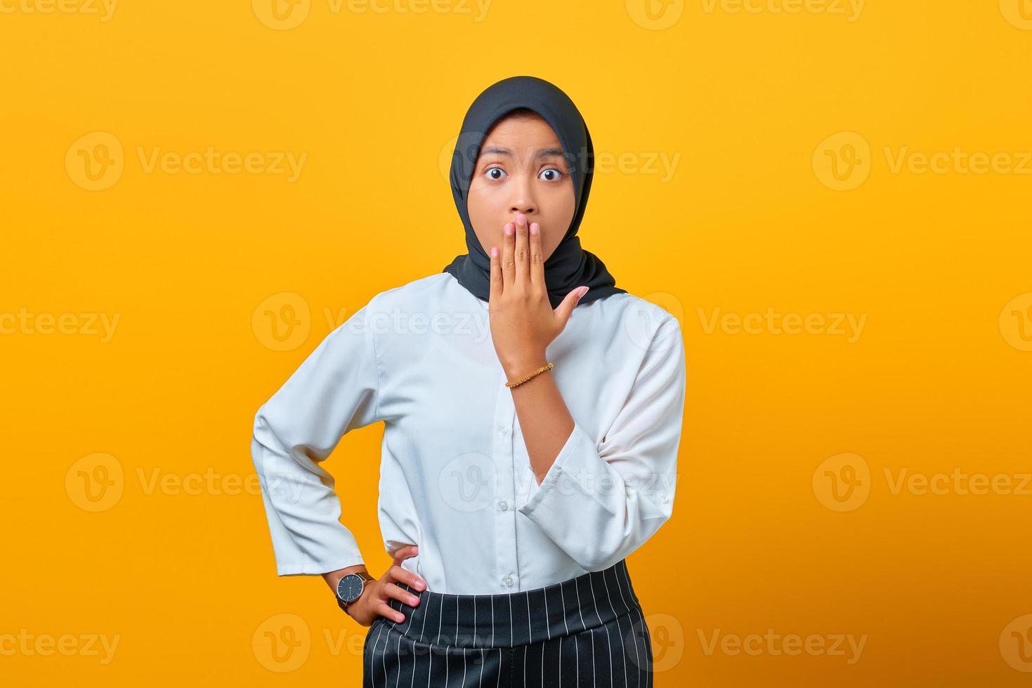 surpris jeune femme asiatique couvrant la bouche avec les mains isolées sur fond jaune photo