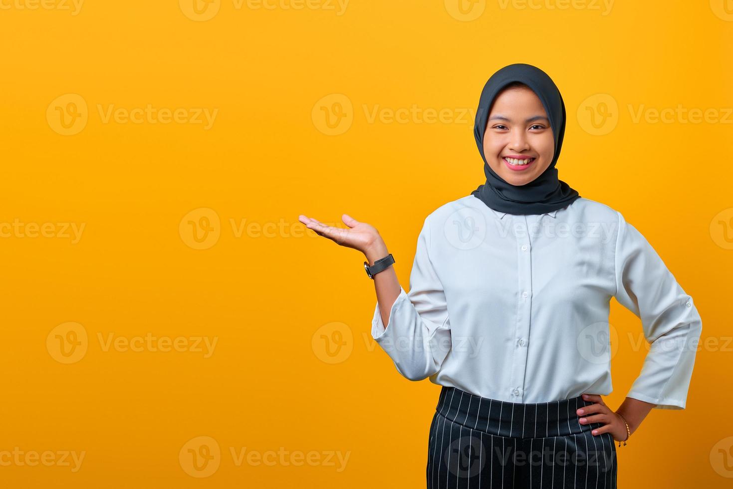 souriante jeune femme asiatique présentant le produit et regardant la caméra sur fond jaune photo