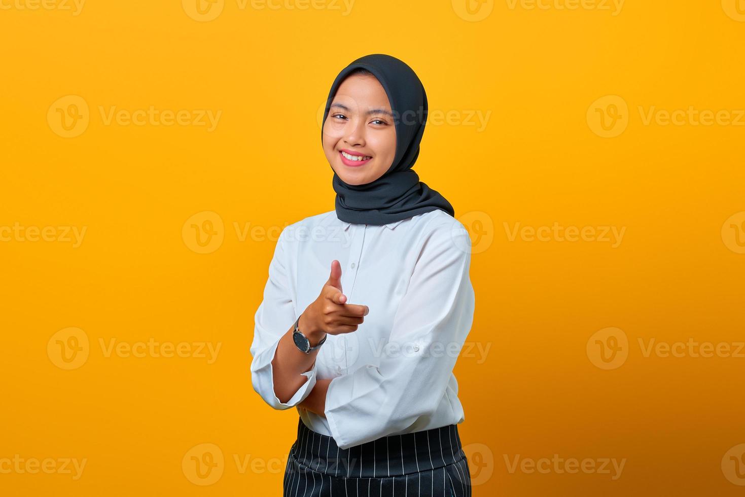 Portrait de jeune femme asiatique souriante pointant du doigt la caméra sur fond jaune photo