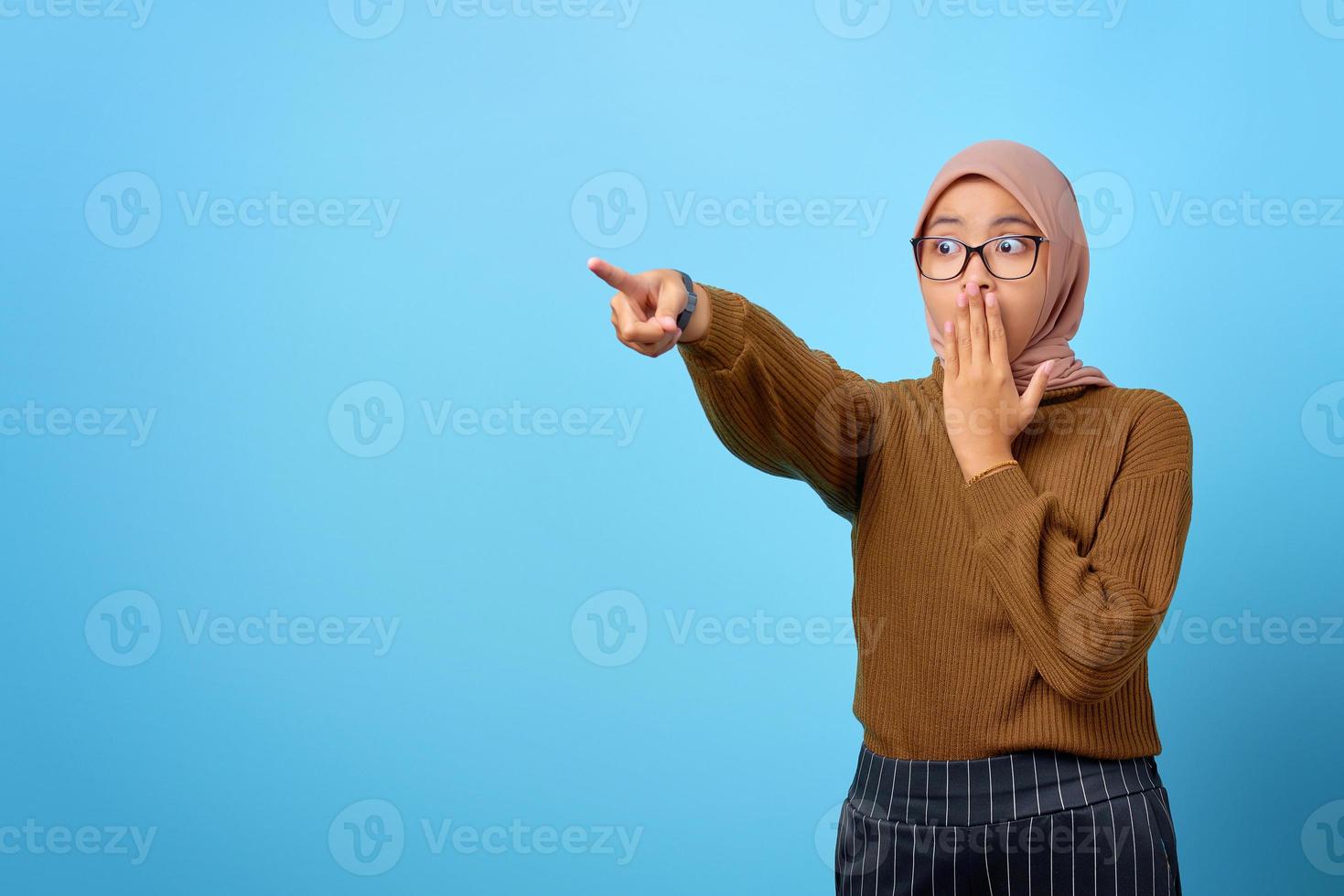 Portrait d'une belle femme asiatique surprise, pointant le doigt pour copier l'espace sur fond bleu photo