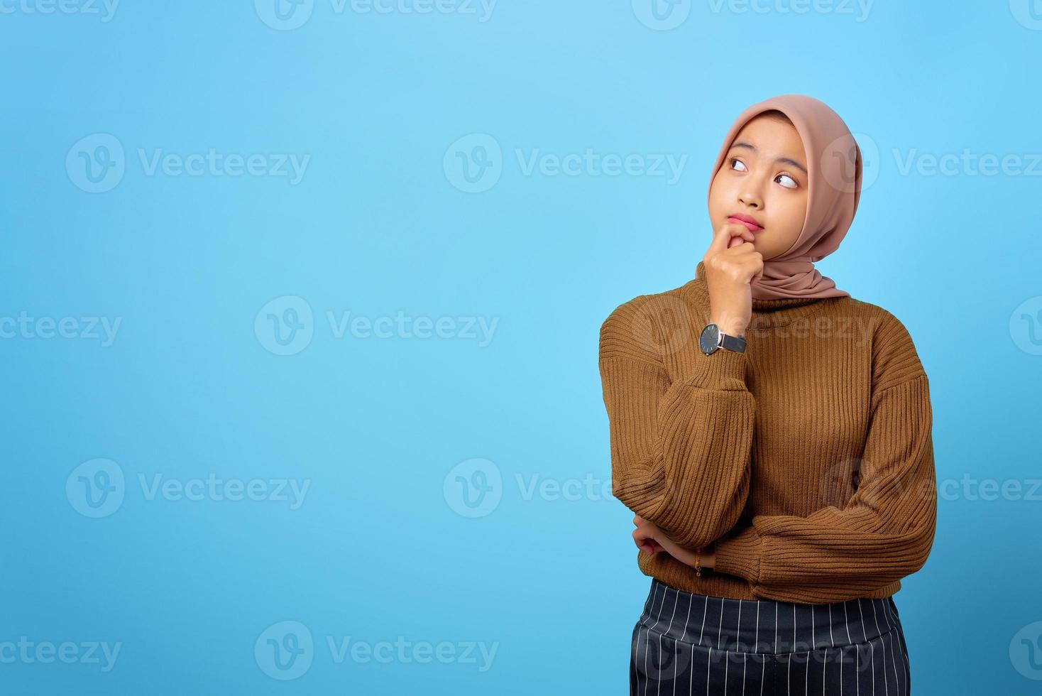 Une jeune femme asiatique pensive a l'air de réfléchir sérieusement à une question sur fond bleu photo