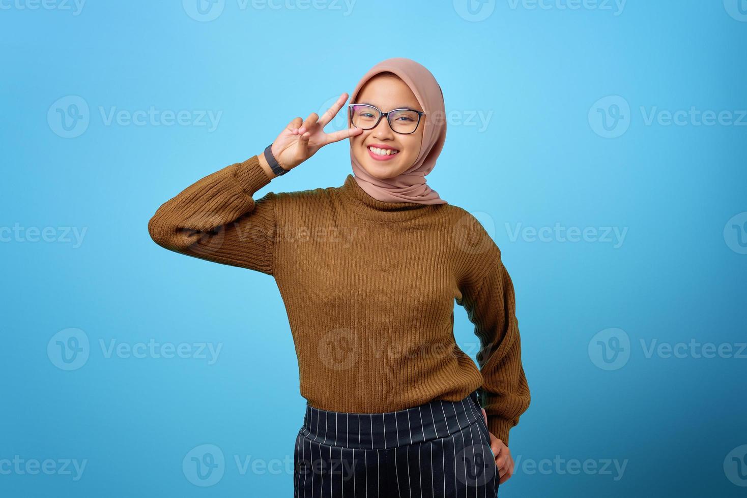 joyeuse jeune femme asiatique montrant le signe de la paix sur les yeux sur fond bleu photo