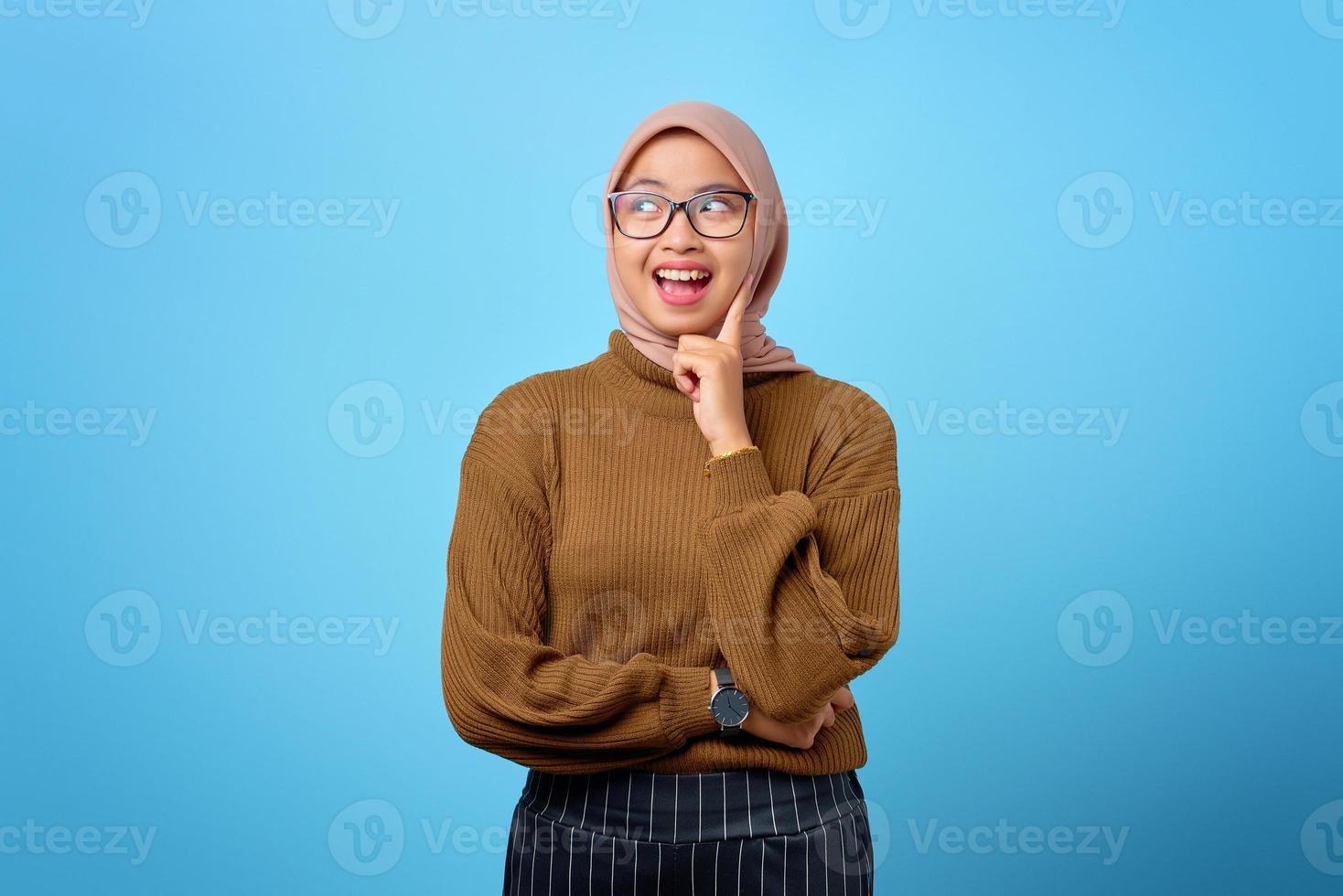 joyeuse jeune femme asiatique touche la joue par les doigts sur fond bleu photo