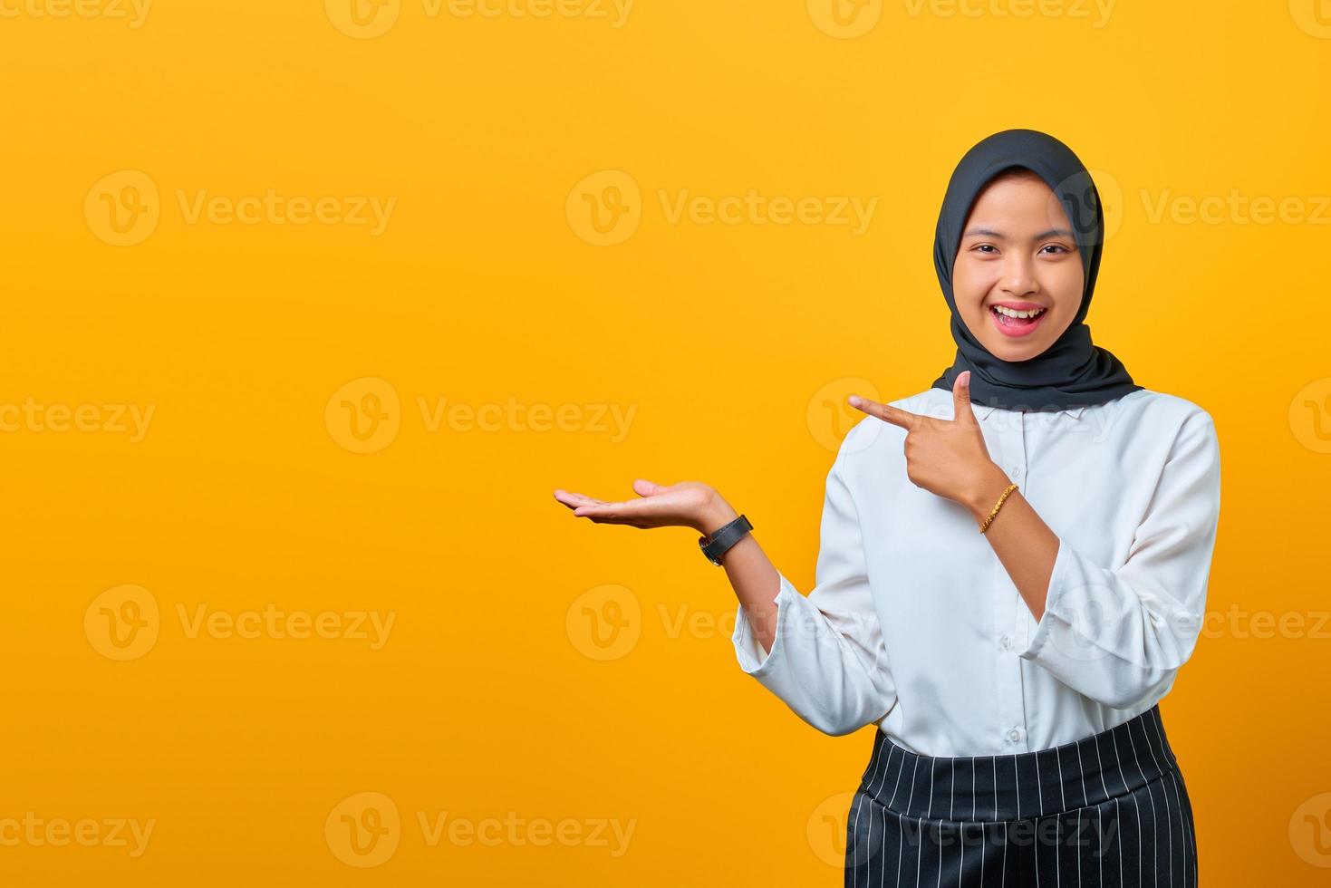 joyeuse jeune femme asiatique présentant le produit et pointant du doigt sur fond jaune photo