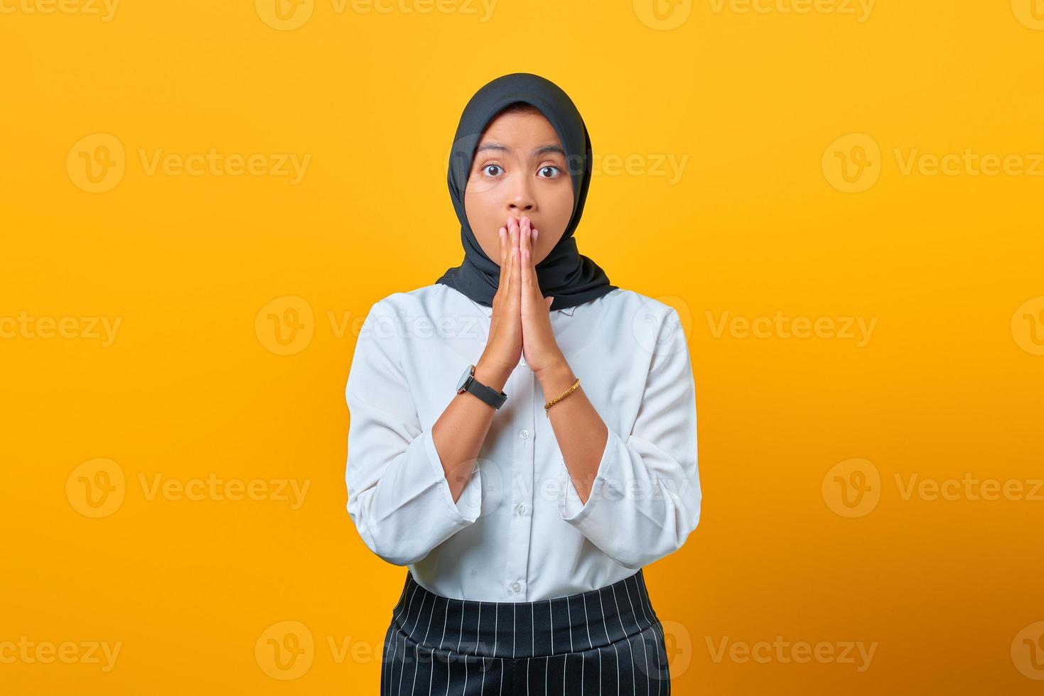 surpris jeune femme asiatique couvrant la bouche avec les mains isolées sur fond jaune photo