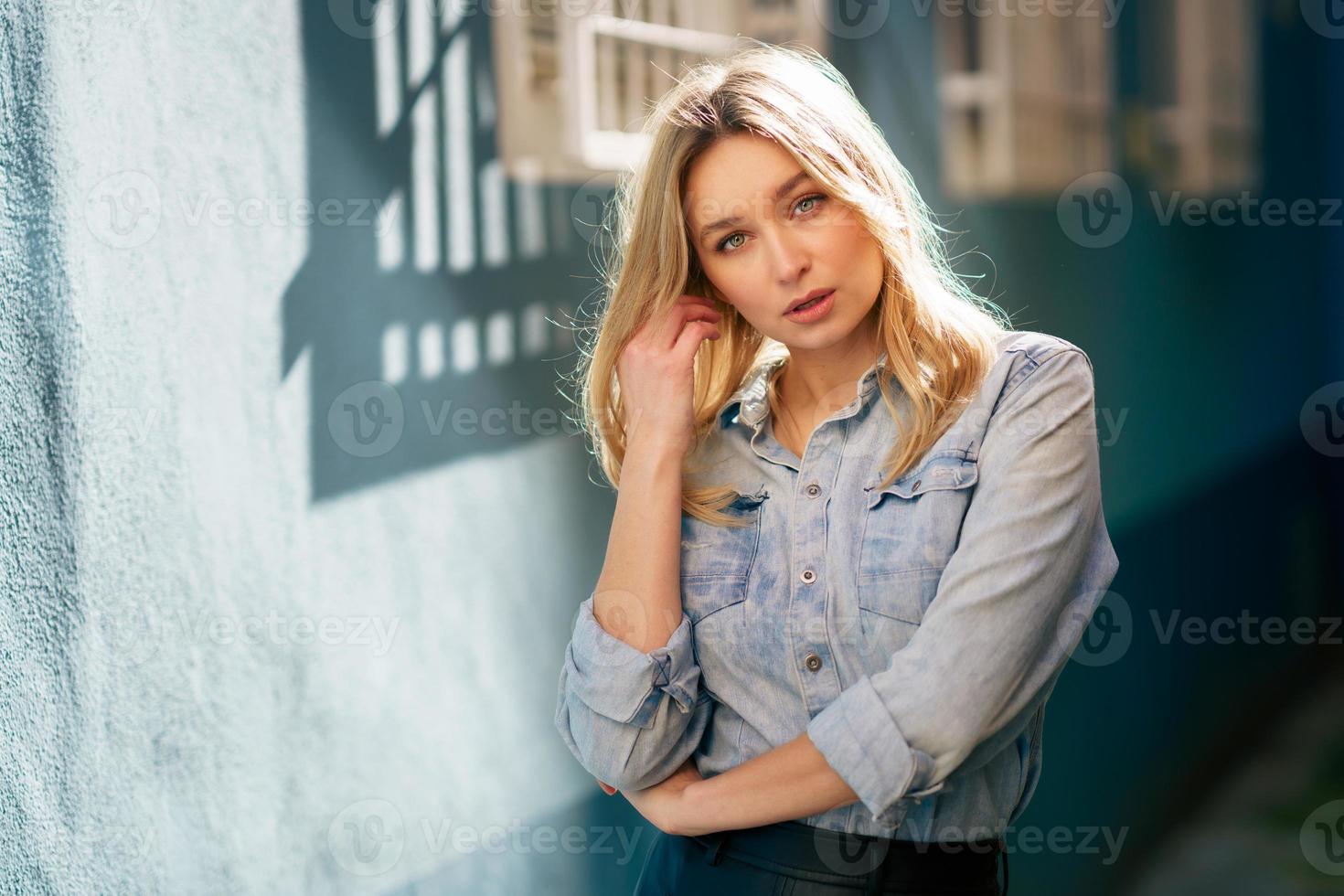 femme blonde portant une chemise en jean et une jupe en cuir noir debout dans la rue. photo