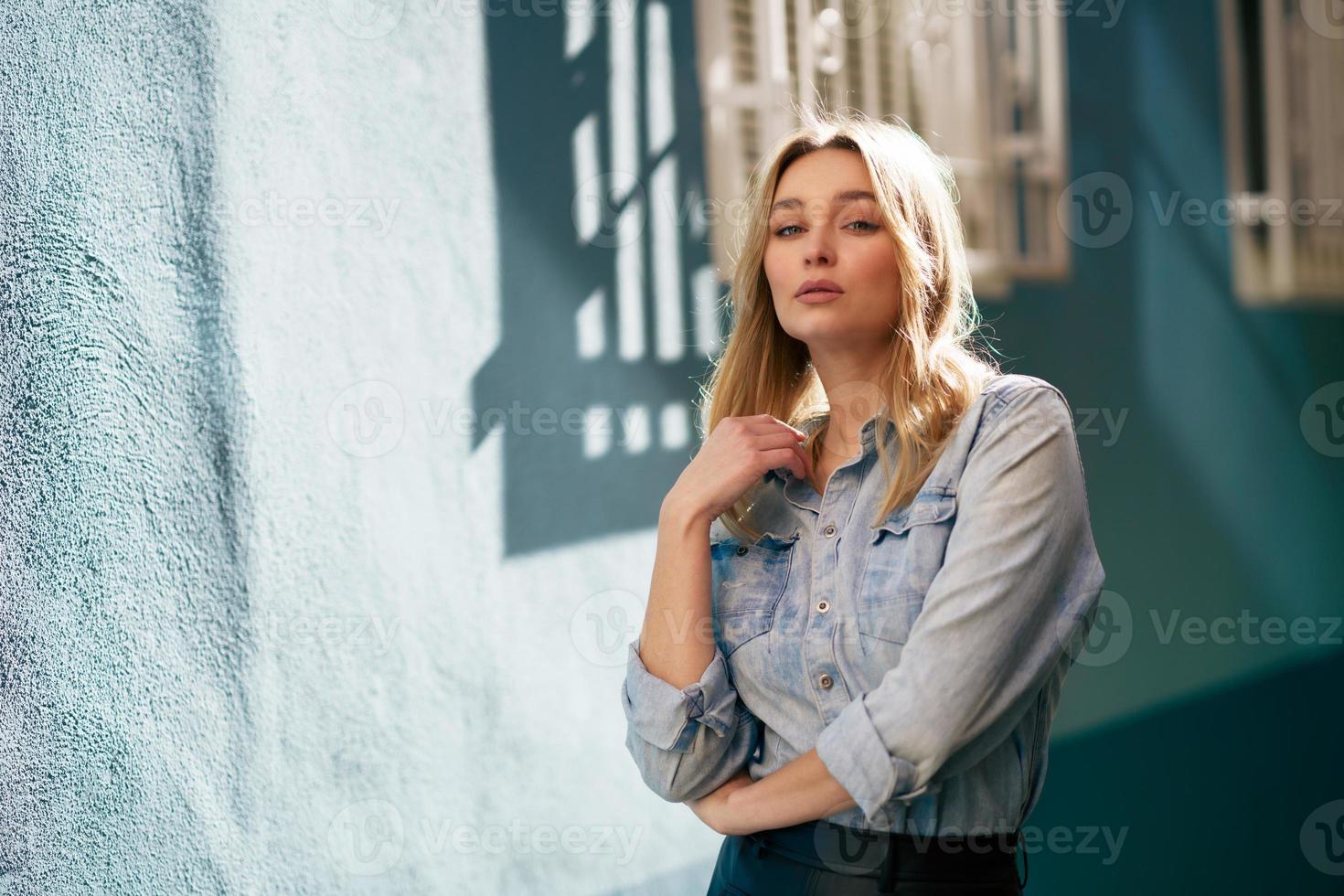 femme blonde portant une chemise en jean et une jupe en cuir noir debout dans la rue. photo