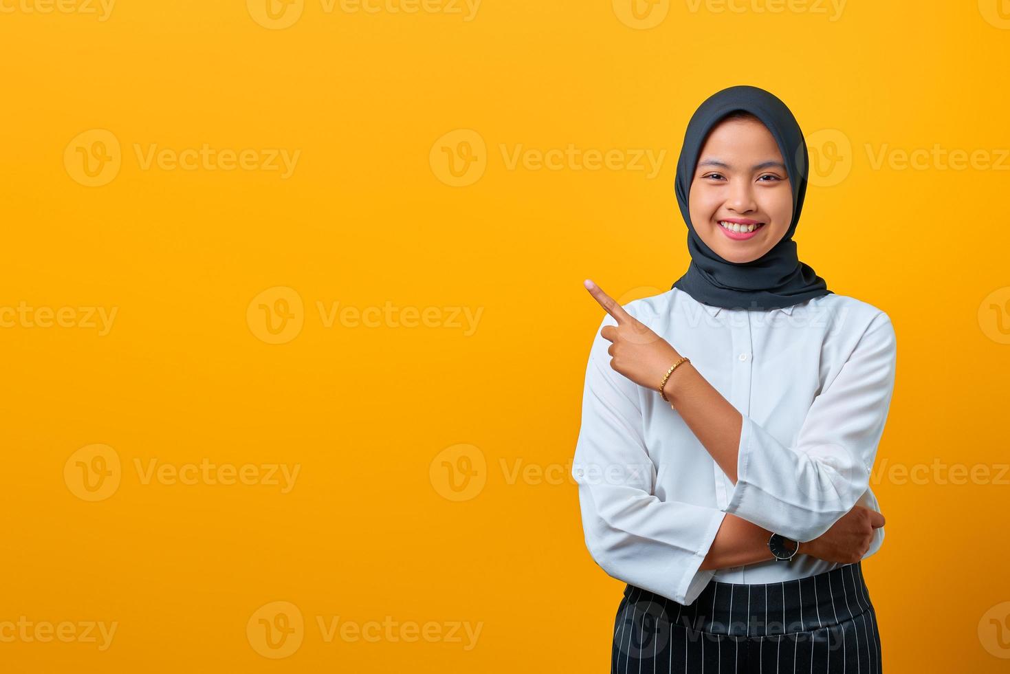 Souriante jeune femme asiatique pointant du doigt l'espace de copie sur fond jaune photo