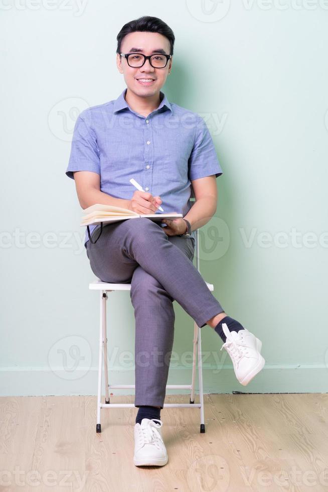 Jeune homme d'affaires asiatique assis sur une chaise en fond vert photo