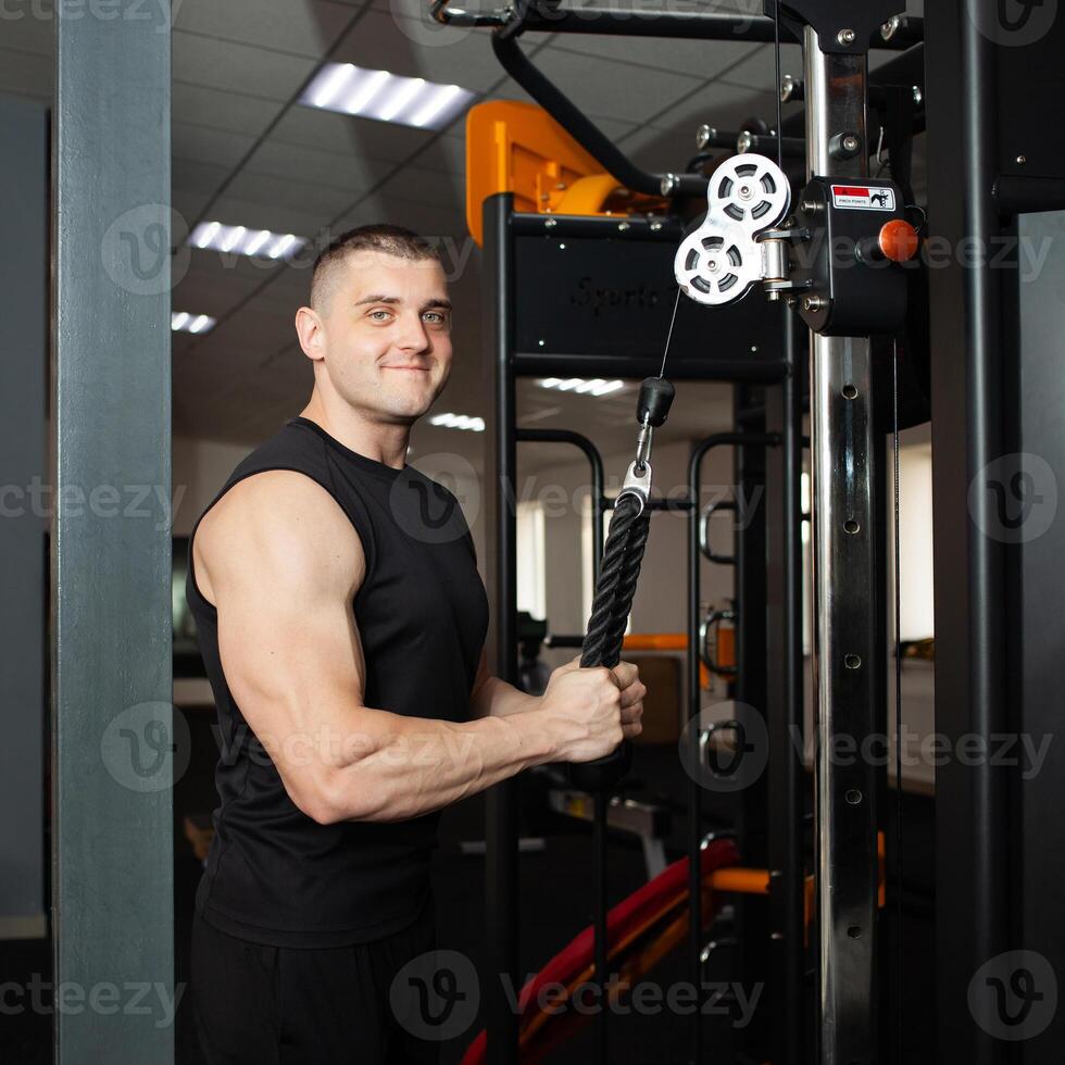 Jeune Beau entraîneur dans une noir uniforme contre Contexte de une simulateur dans salle de sport. musclé athlétique corps de une carrossier, encadrement, individuel des sports et poids perte cours. portrait. photo