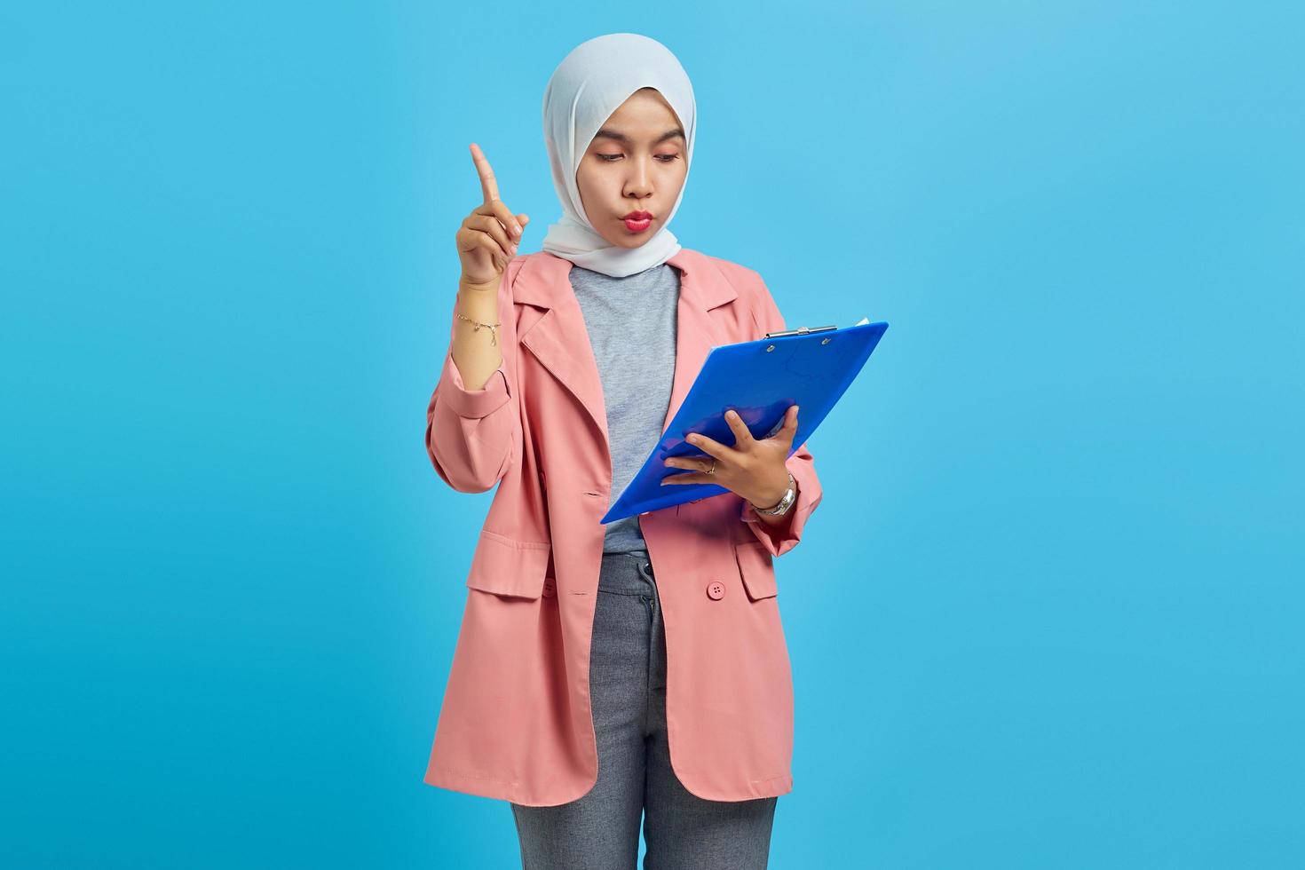 portrait d'une belle femme tenant un presse-papiers debout et pointant vers le haut sur fond bleu photo