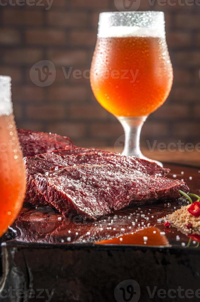 steak de denver grillé tranché sur une planche à découper en bois avec du sel de parrilla et deux verres de bière en sueur. viande de boeuf en marbre - gros plan. photo