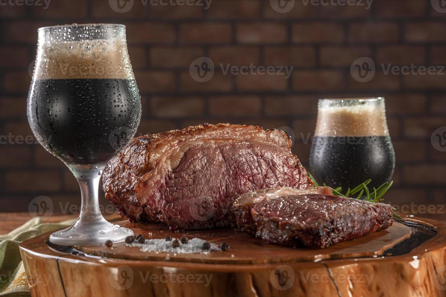 contre-filet grillé sur une planche à découper en bois avec deux verres de tulipe en sueur de bière pression noire. photo