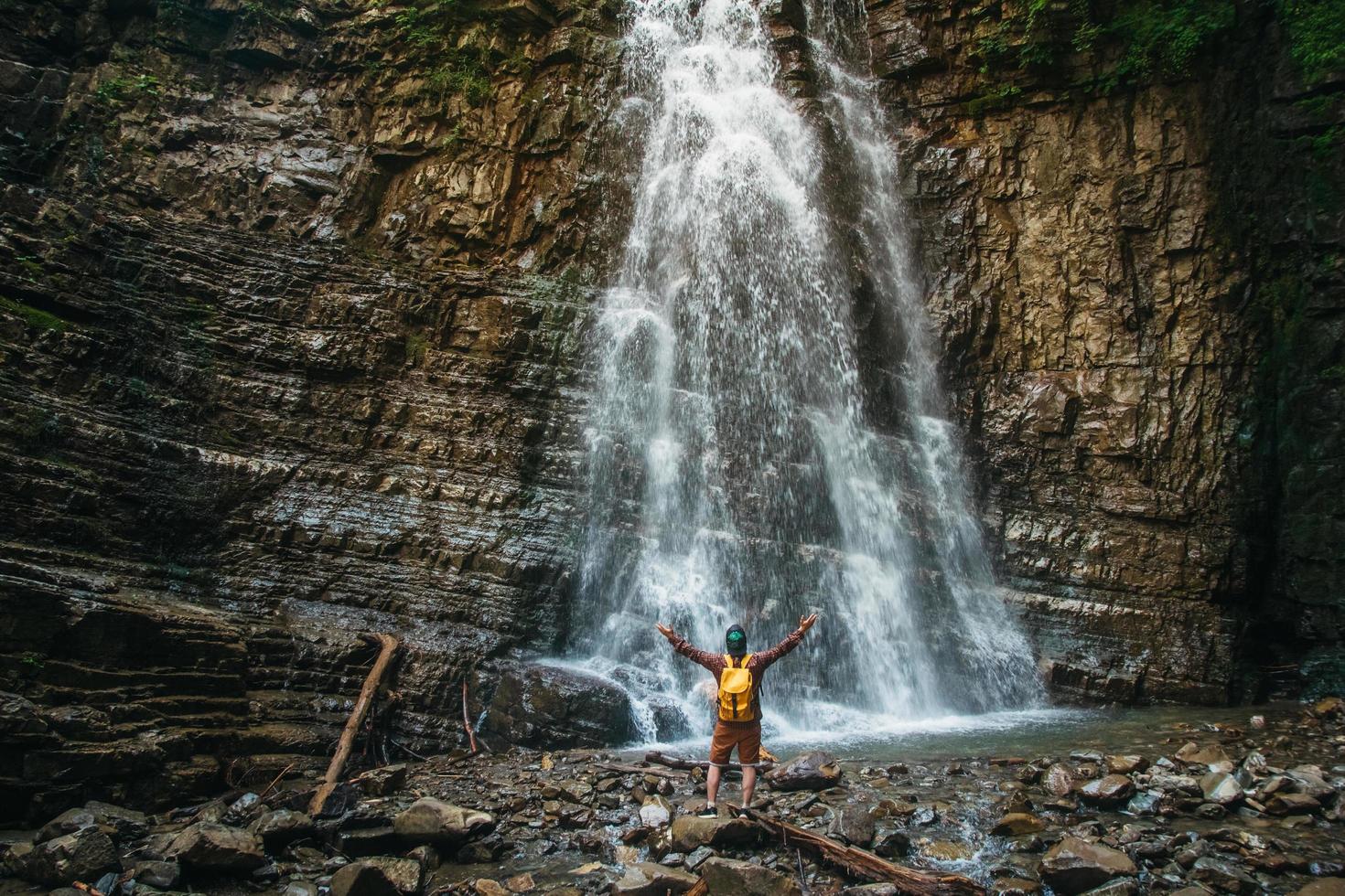 homme voyageur avec un sac à dos jaune debout sur fond d'une cascade. concept de mode de vie de voyage. photo