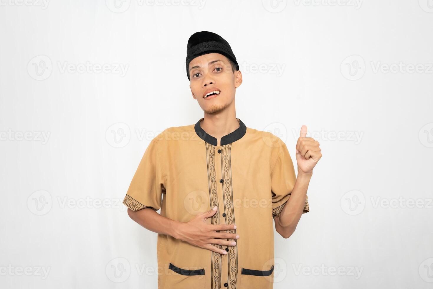 asiatique musulman homme portant musulman vêtements souriant Heureusement, les pouces en haut geste tandis que en portant une en bonne santé ou plein estomac. isolé blanc Contexte. photo