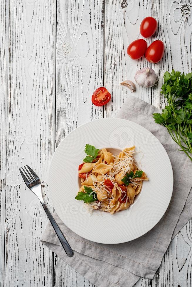 pâtes conchiglioni aux tomates cerises, fromage et persil en plaque blanche sur fond de bois photo