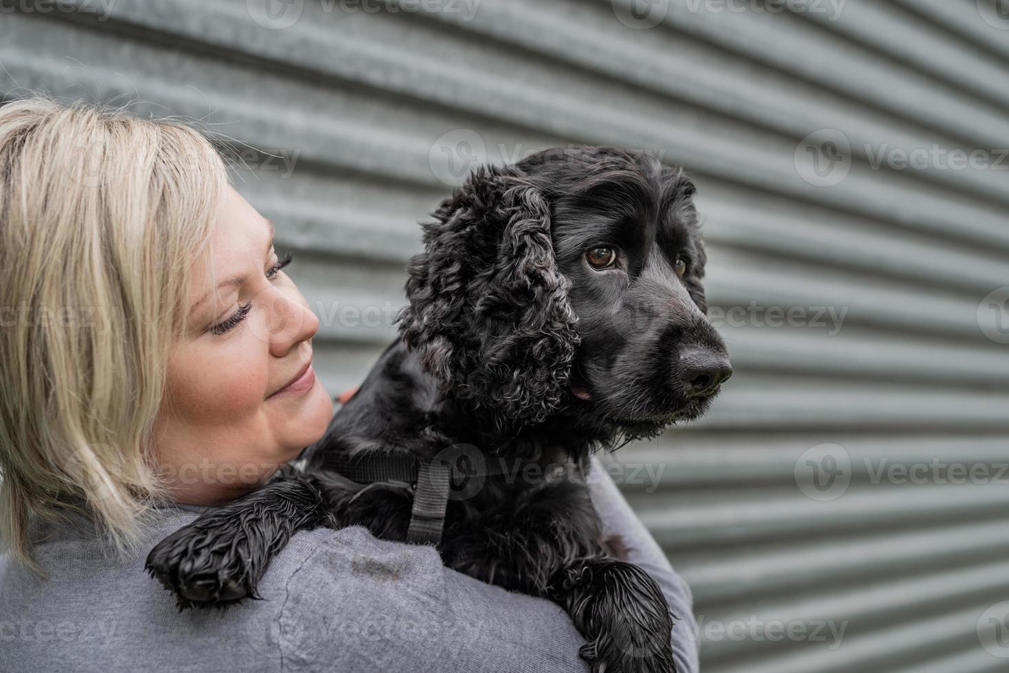 Jeune femme tenant son chien cocker sur fond de mur gris à l'extérieur photo