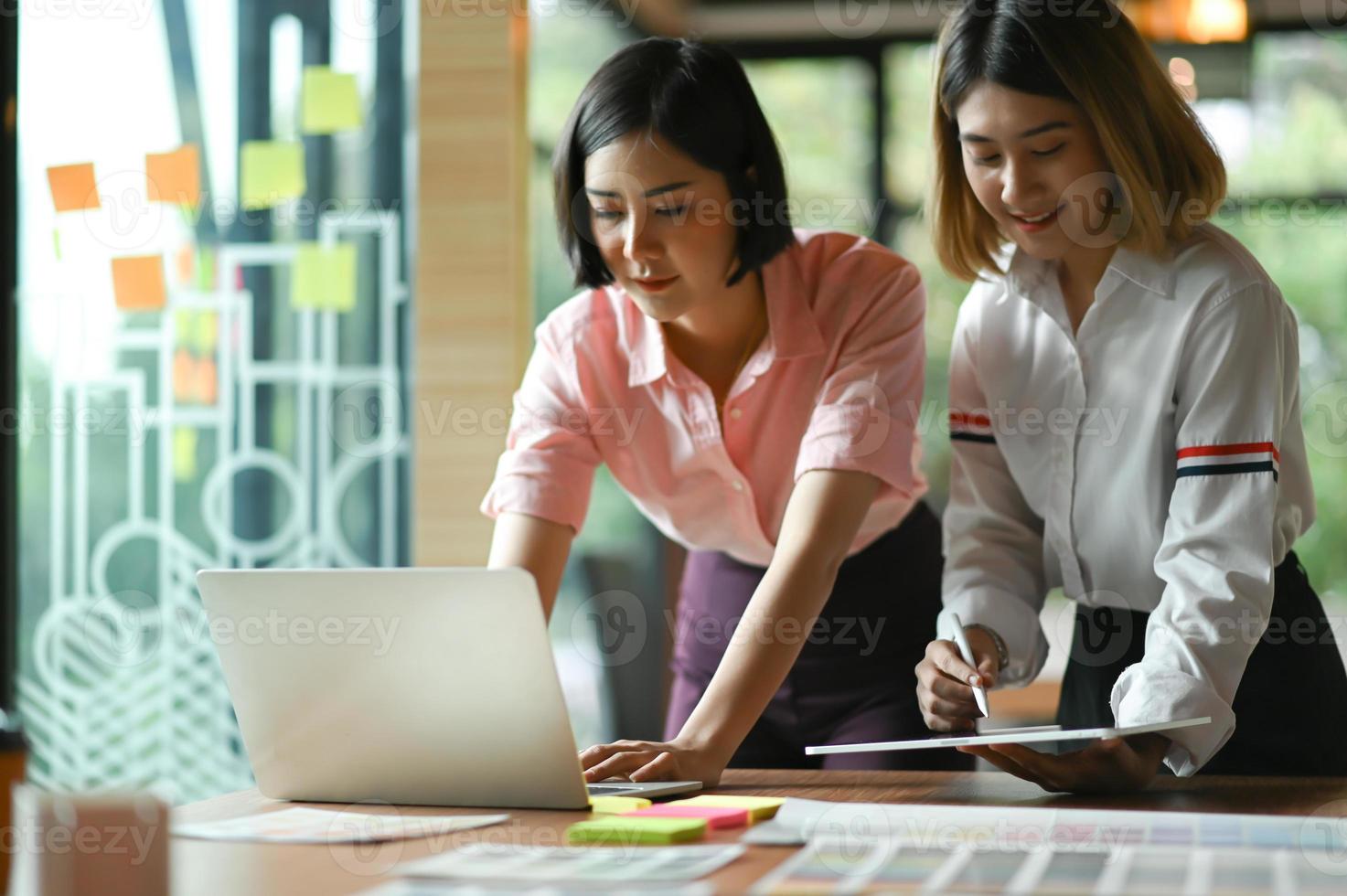 graphiste asiatique travaillant ensemble au bureau, elles utilisent un ordinateur portable et une tablette. photo