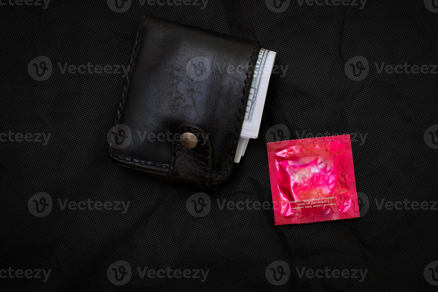 Portefeuille en cuir noir gros plan avec un préservatif rouge sur fond noir photo