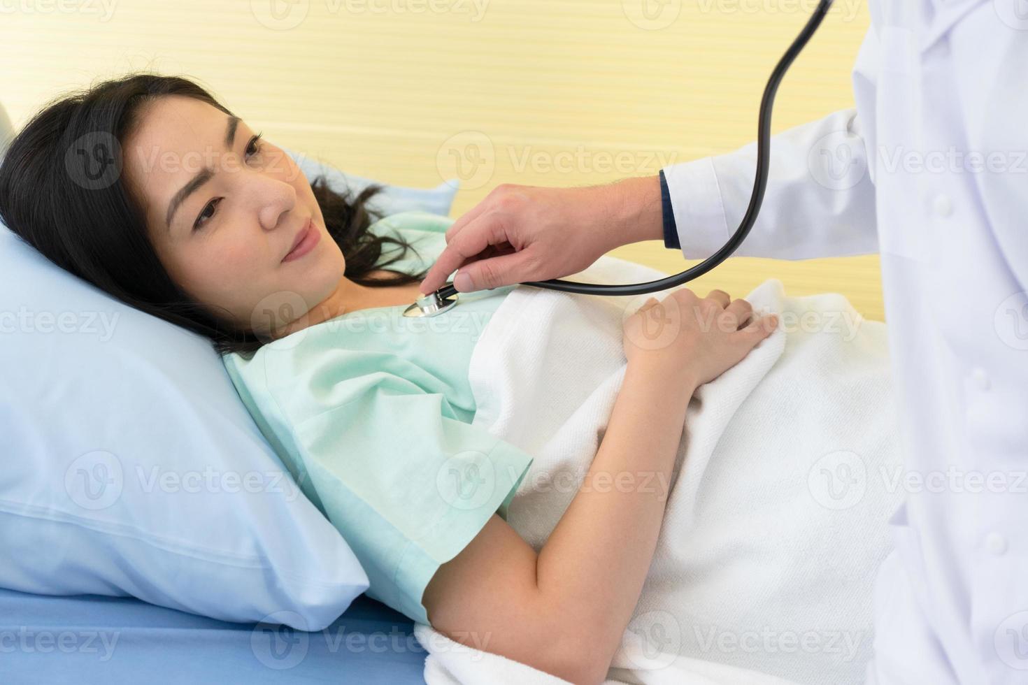 médecin utilisant un stéthoscope pour écouter les sons pulmonaires et cardiaques d'une femme asiatique malade et allongée dans un lit d'hôpital. concept de soins de santé et médical photo