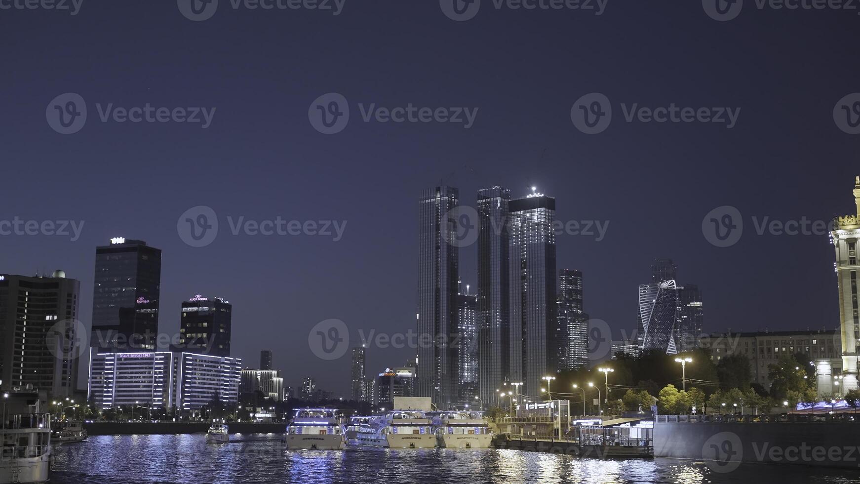 Urbain rivière avec navires embrasé moderne ville. action. magnifique grattes ciels de moderne ville lueur à nuit par rivière. flottant navires sur rivière avec ville paysage à nuit photo