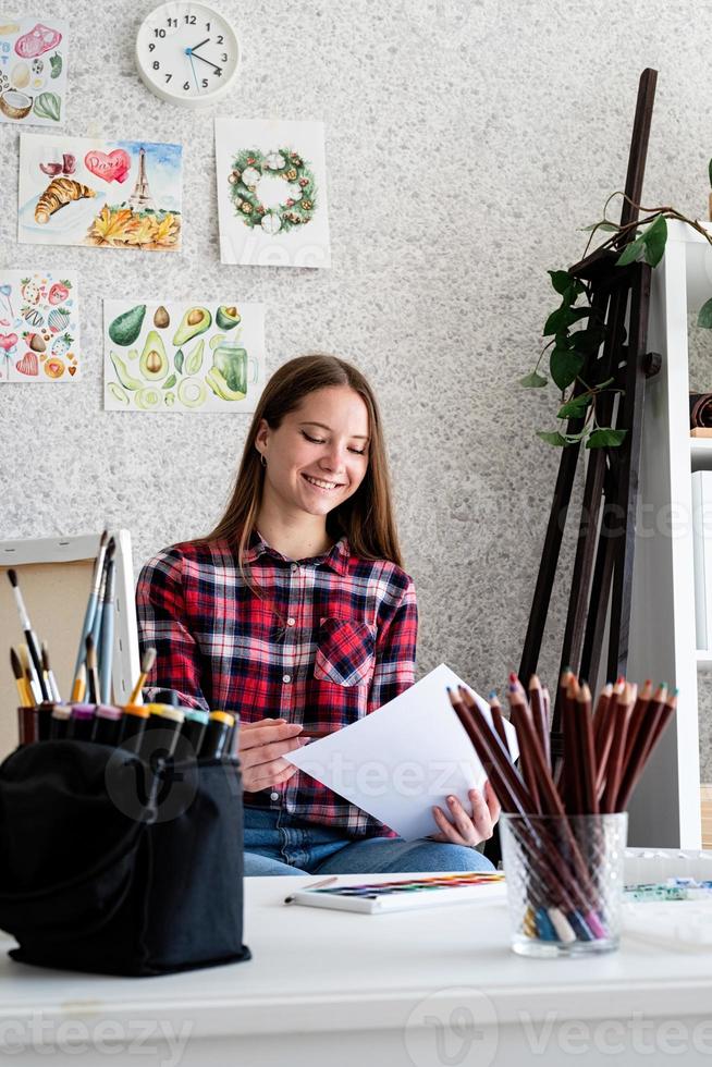 belle femme artiste en chemise à carreaux peignant une photo à la maison