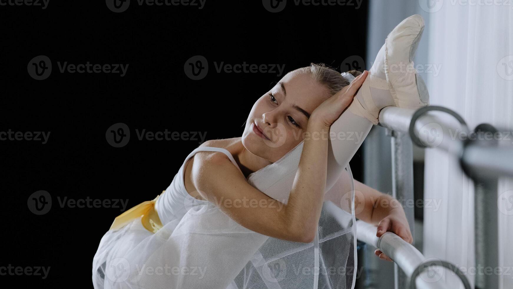 souple ballerine fille enfant dans ballet tutu s'étire près barre dans Danse classe élongation jambes avec plaisir facile souplesse jouit entraine toi formation prépare pour performance repose avec fermé yeux photo