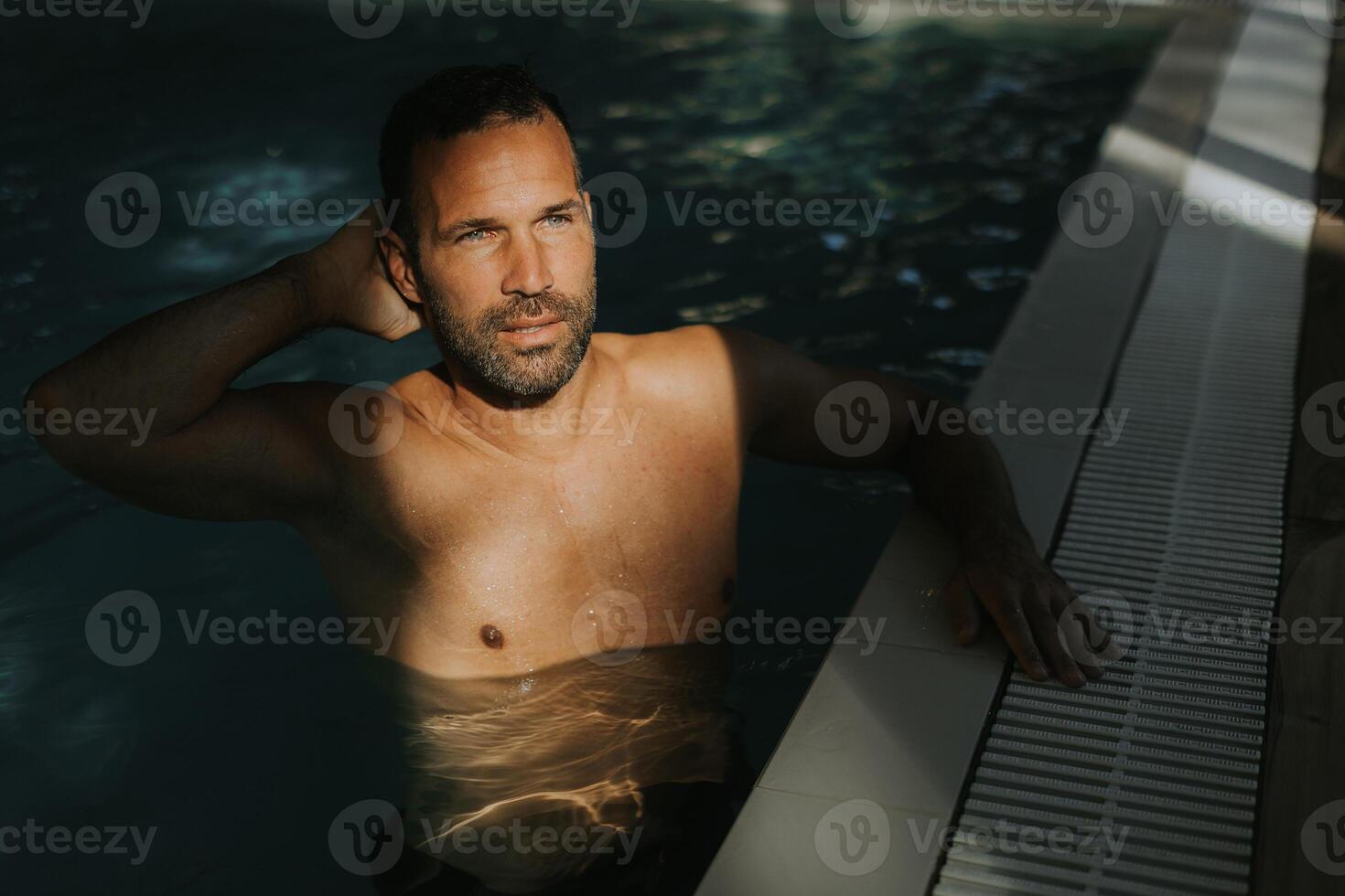 Beau Jeune homme relaxant sur le bord de intérieur nager bassin photo
