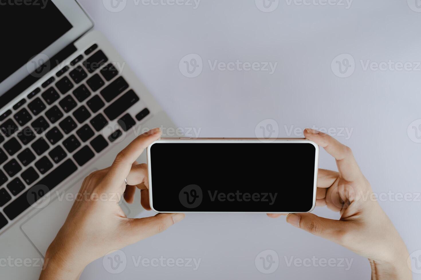 Haut vue de main en portant téléphone intelligent avec Vide noir écran et ordinateur portable sur blanc Bureau bureau photo