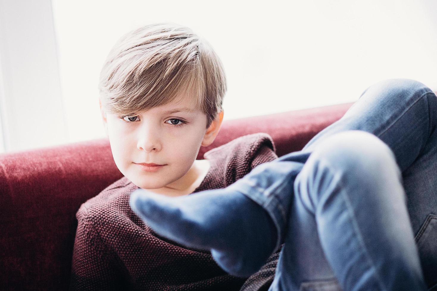 enfant mignon garçon assis sur un canapé, les jambes croisées photo