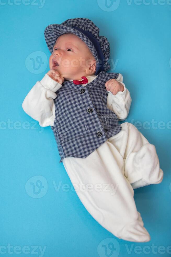 nouveau née marrant bébé dans plein croissance dans une magnifique costume et chapeau sur une bleu Contexte. photo