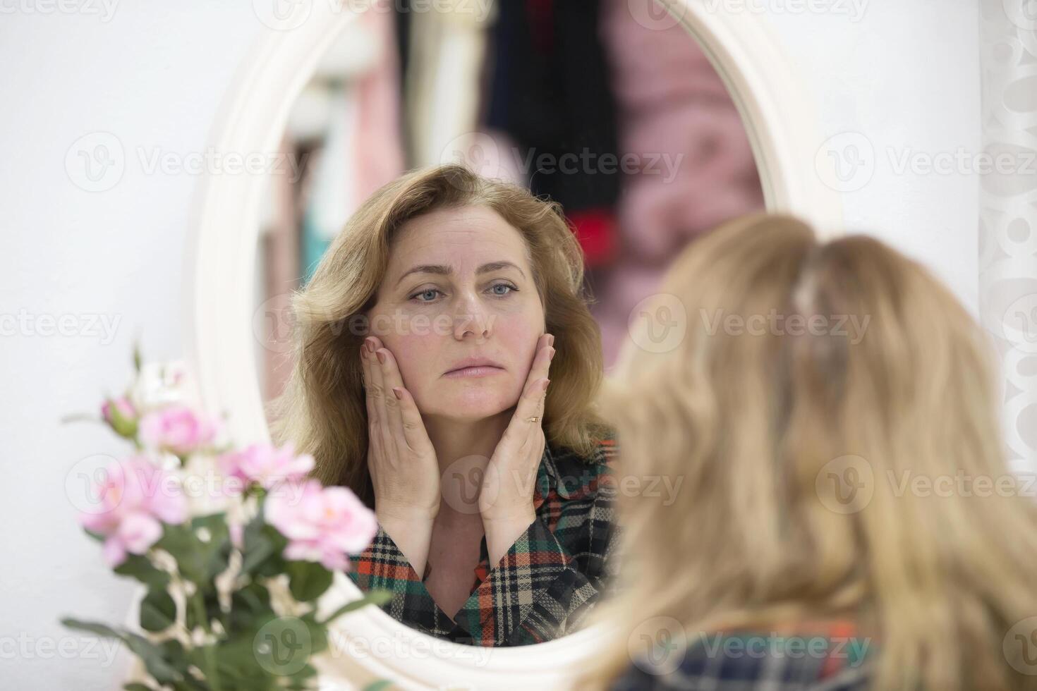 un personnes âgées femme regards dans le miroir à le les rides. femme touche sa vieilli visage photo