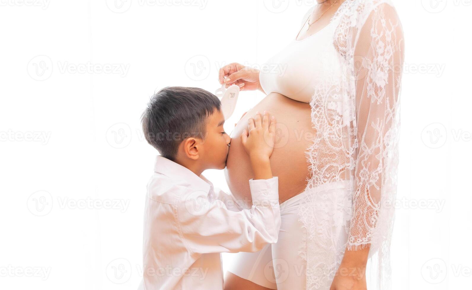 Jeune garçon est embrasser le Enceinte femme isolé sur blanc Contexte photo