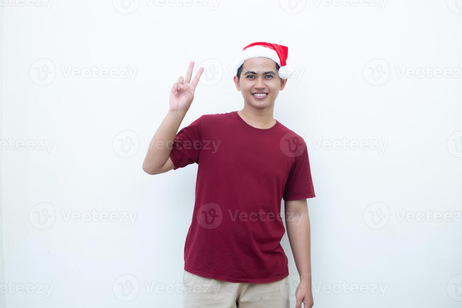 Jeune asiatique homme portant une Père Noël claus chapeau souriant, choc et montrer du doigt à sa côté isolé par blanc Contexte pour visuel la communication photo