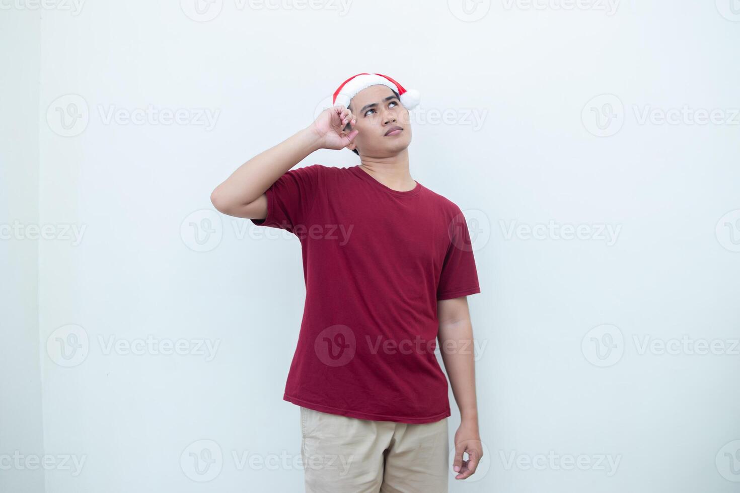 Jeune asiatique homme portant une Père Noël claus chapeau exprimer confusion, pensée, et puis ayant un idée, isolé par une blanc Contexte pour visuel la communication photo