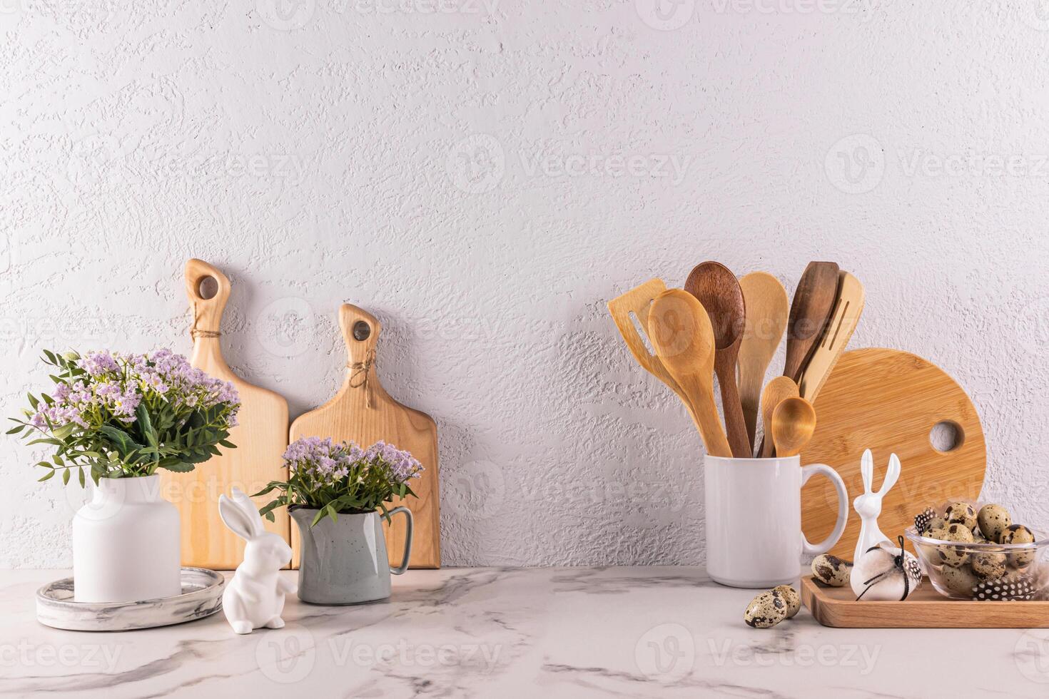 en bois cuisine ustensiles fabriqué de respectueux de la nature matériaux, printemps fleurs dans une vase et cruche, Pâques lapin figurines sur une marbre comptoir. de face voir. photo