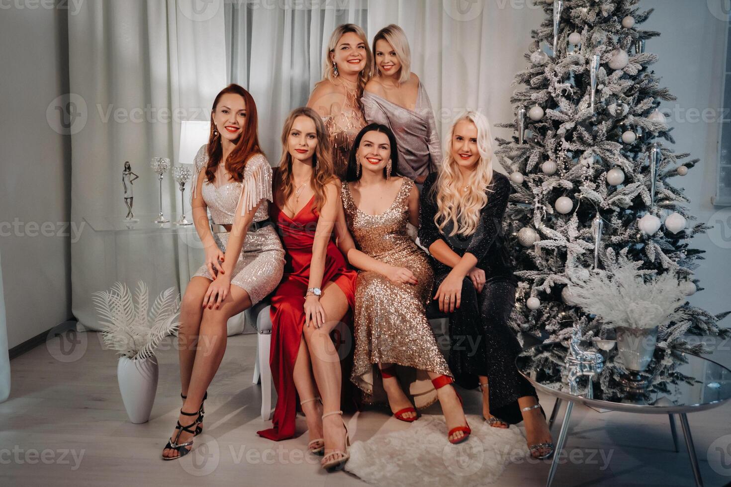 sexy femmes dans Robes sont séance sur le canapé près le Noël arbre dans le intérieur de le maison photo