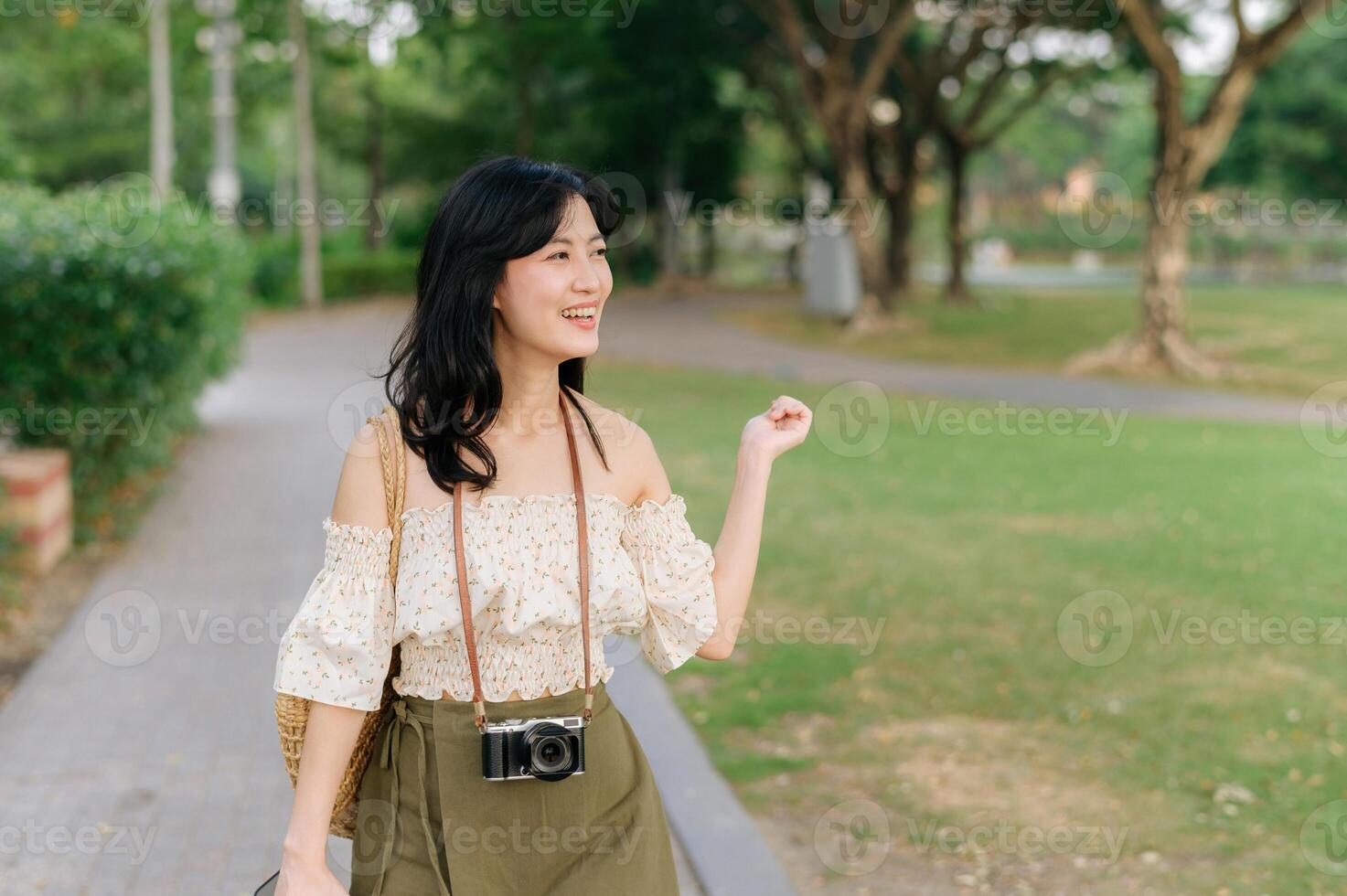 portrait de asiatique Jeune femme voyageur avec tissage chapeau et panier et une caméra sur vert Publique parc la nature Contexte. périple voyage mode de vie, monde Voyage explorateur ou Asie été tourisme concept. photo