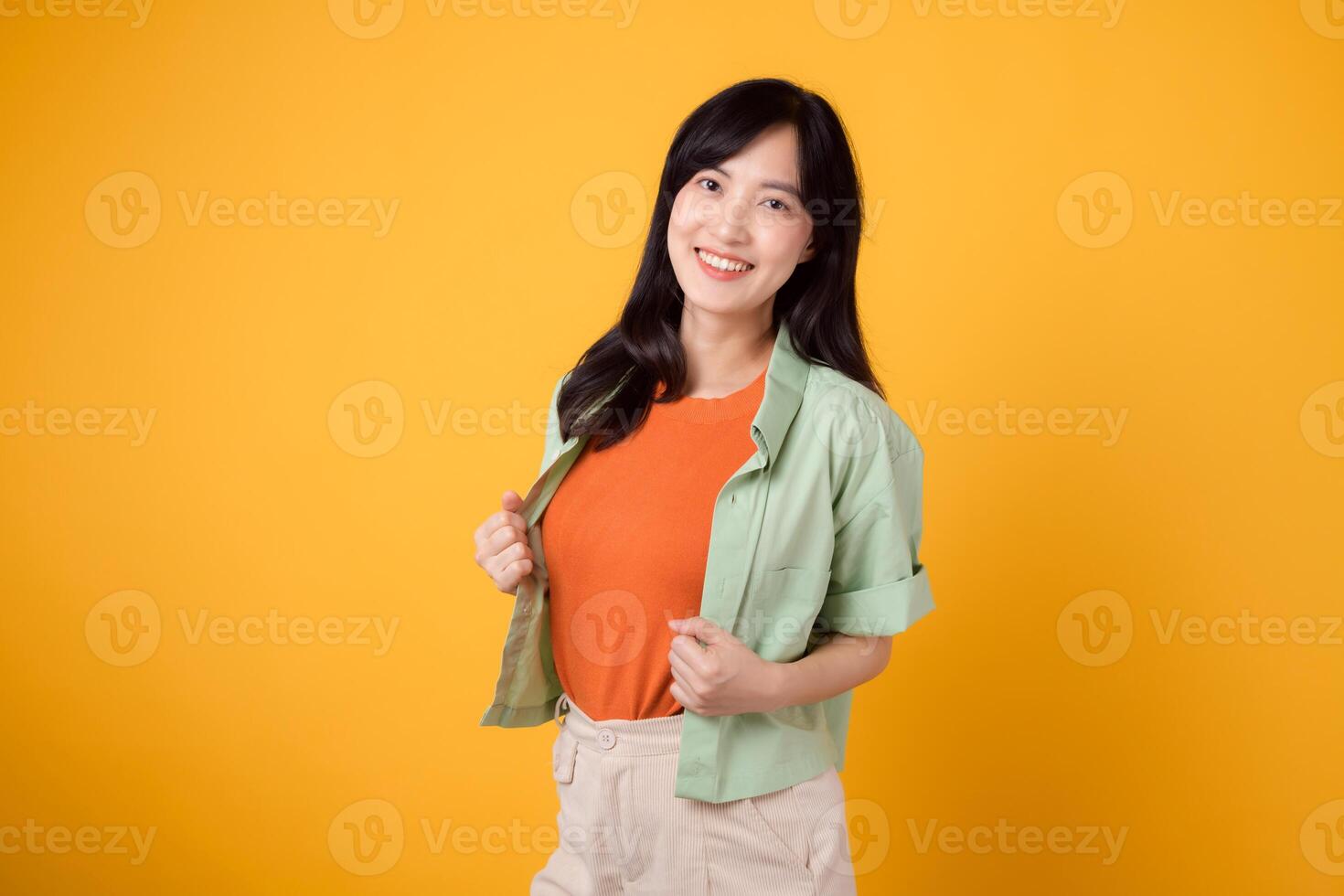 éclat de bonheur et bien-être avec une de bonne humeur Jeune asiatique femme 30s portant un Orange chemise. sa content esprit bien-être geste sur Jaune Contexte reflète une captivant bonheur portrait. photo