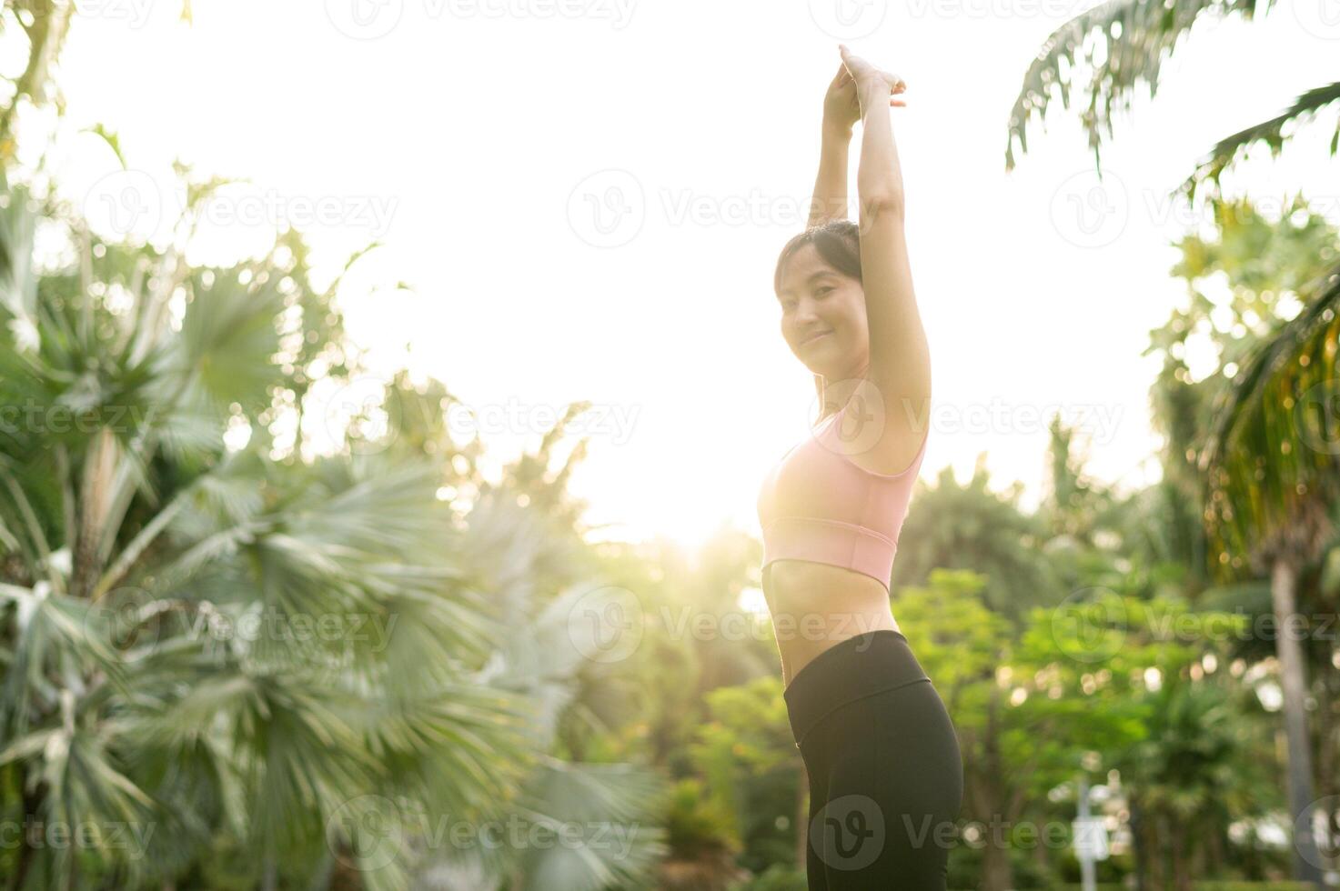 en forme 30s Jeune asiatique femme dans rose tenue de sport pièces yoga et s'étire muscles. embrasse en bonne santé Extérieur mode de vie avec aptitude yoga fille dans Publique parc à le coucher du soleil. bien-être et bien étant concept. photo