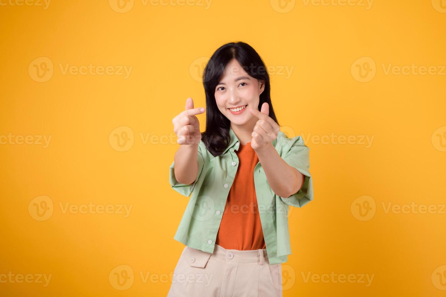 bonheur avec une Jeune asiatique femme dans sa 30s, habillé dans un Orange chemise et vert sauteur. sa mini cœur geste et doux sourire Express une profond message par corps langue. photo