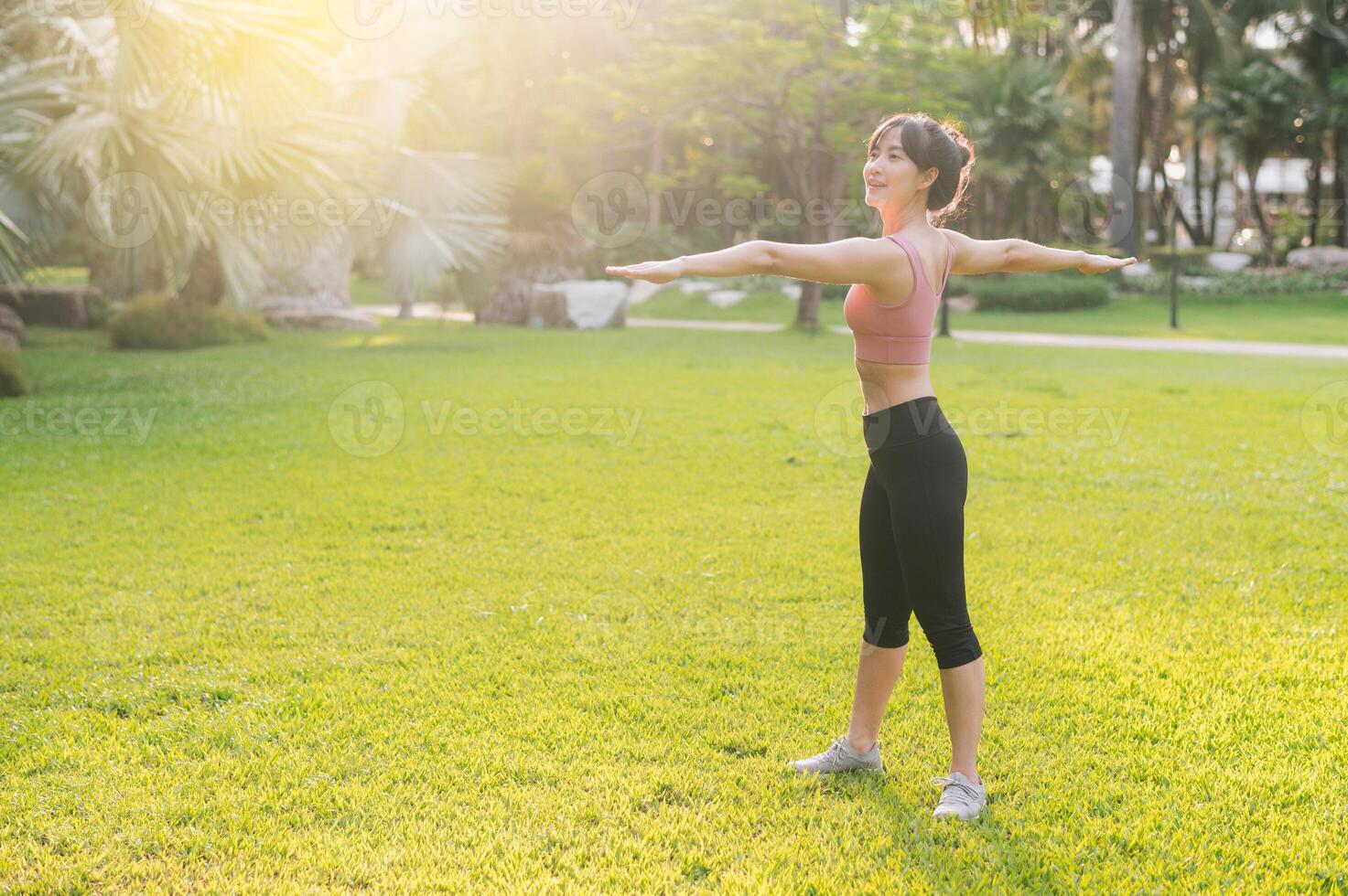 femelle joggeur. en forme 30s Jeune asiatique femme dans rose tenue de sport en train de préparer chaud en haut corps dans parc avant courir. en bonne santé Extérieur mode de vie avec aptitude coureur fille dans le coucher du soleil. concept de bien-être et bien-être photo