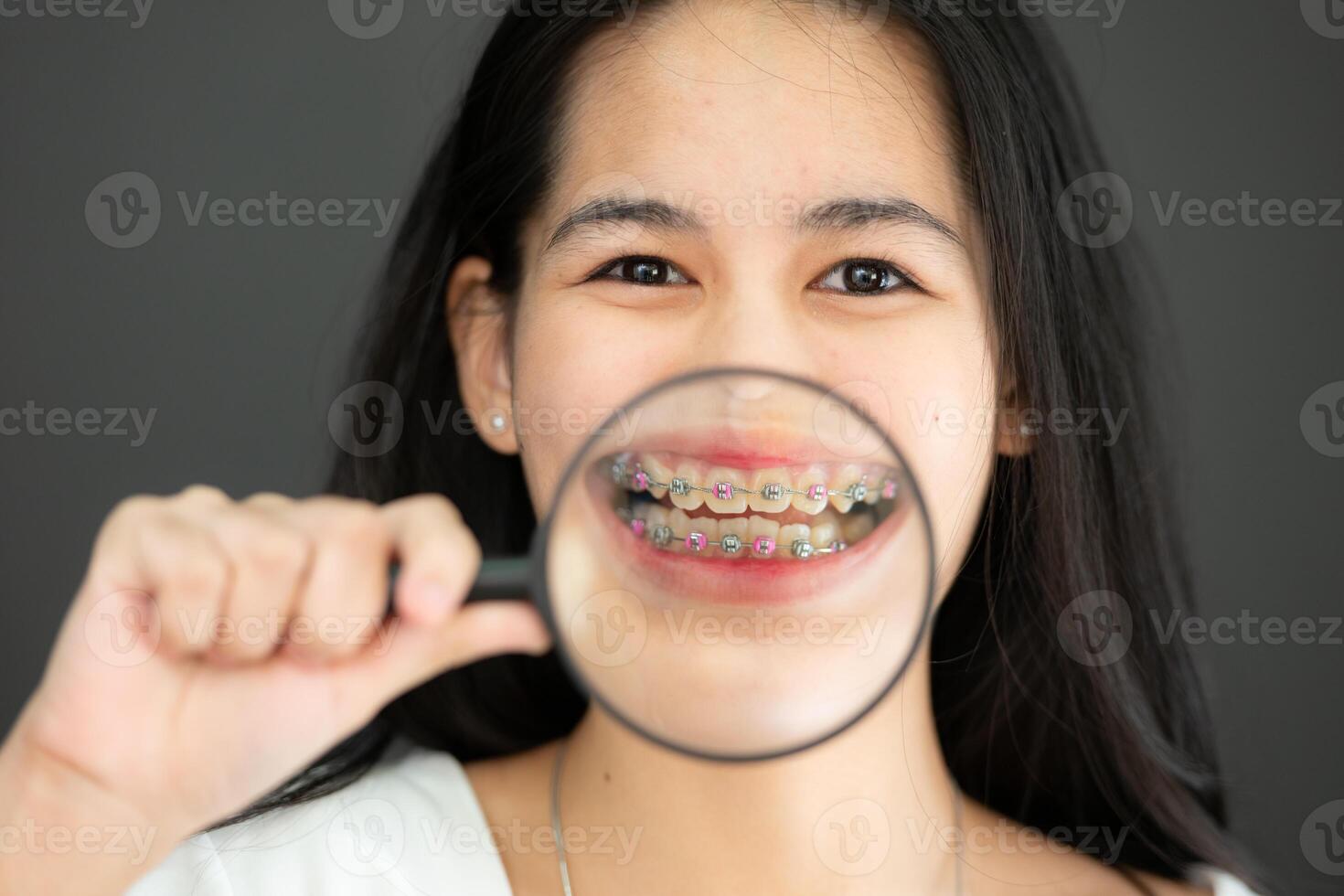 portrait de asiatique Jeune femme dans Vide blanc T-shirt sur noir Contexte avec un appareil dentaire et grossissant verre photo